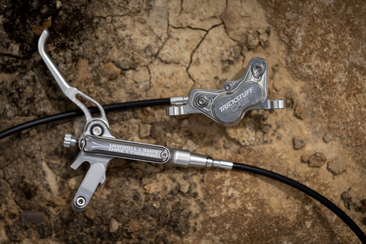 Silver Trickstuff Direttissima lever and C42 caliper linked by black brake hose on rock.