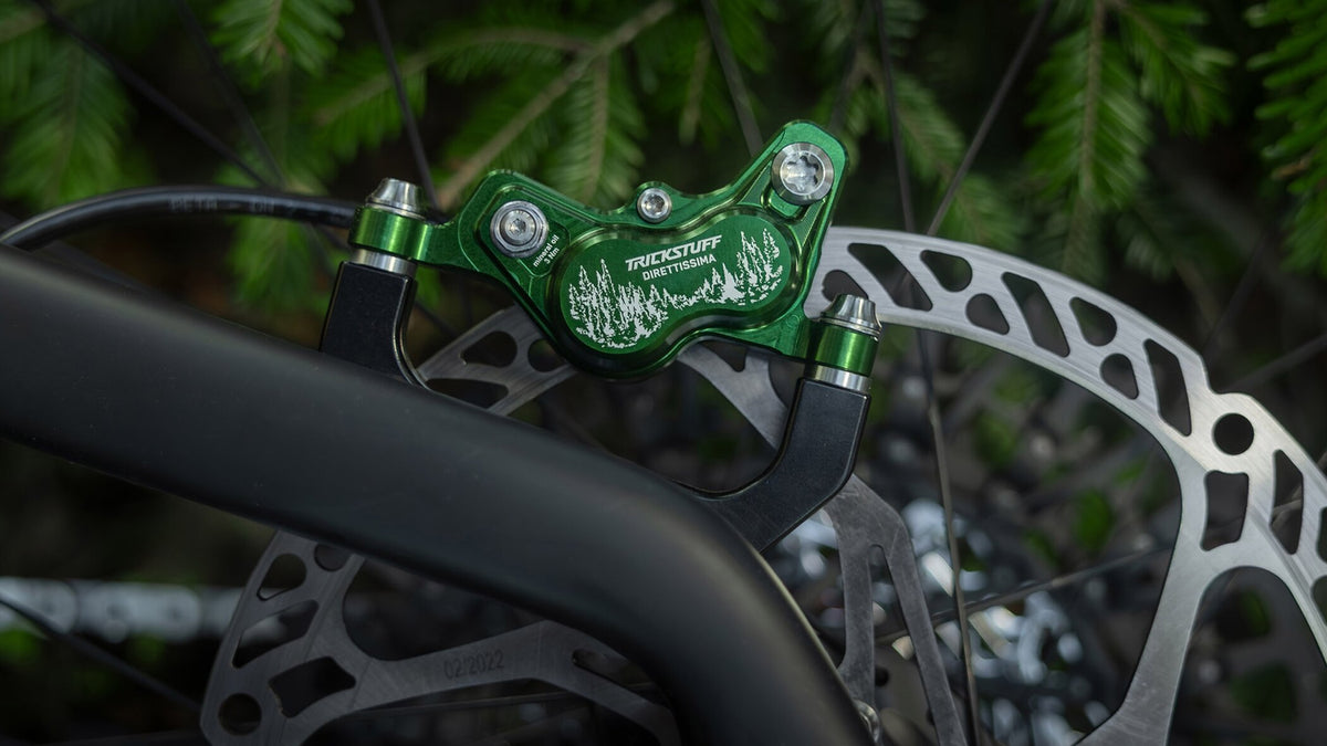 Green Trickstuff Direttissima caliper with a forest graphic mounted beside a disc rotor.