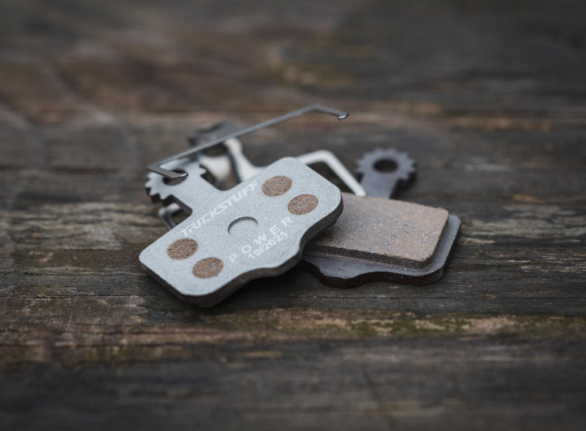 Trickstuff POWER ALU 830 brake pads and spring on wood, showing the backing and friction faces.